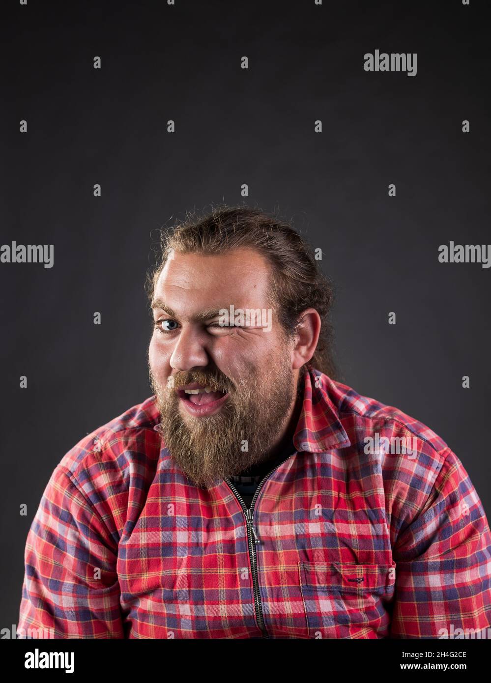 Funny guy with long hair and beard, wearing plaid shirt winking with