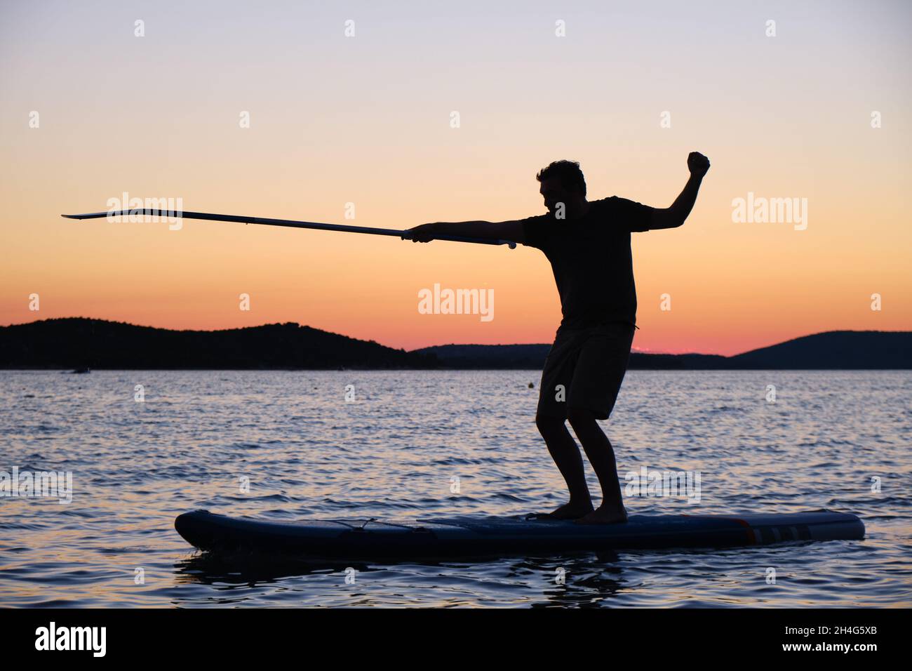 Silhouette of man on stand up paddleboard at sunset, pointing the