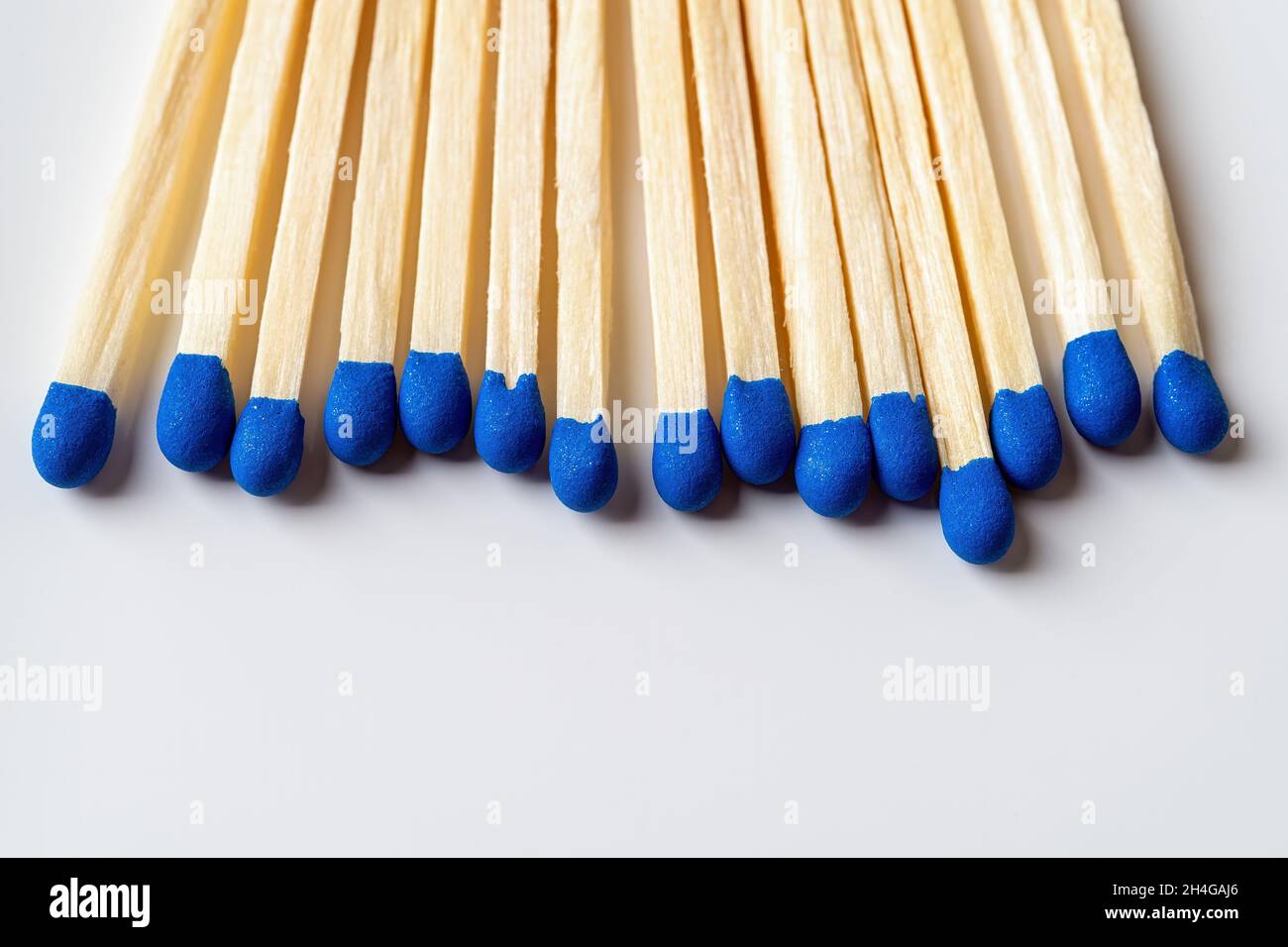 Bright blue wooden matches as a background with copy space. Row of matchsticks with blue heads over light gray surface. Several wooden matches. Stock Photo