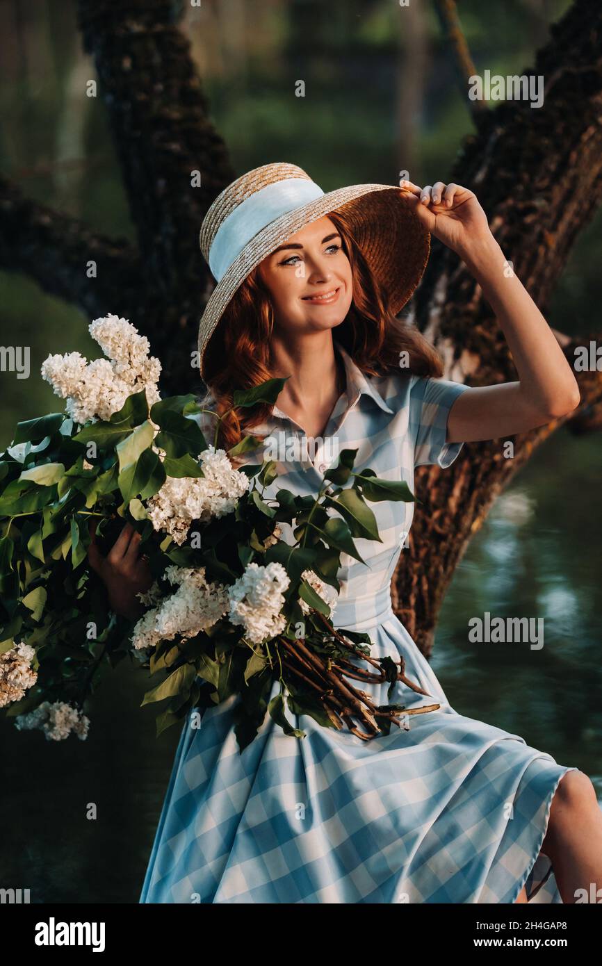 Portrait of a beautiful girl with long hair, a straw hat and a long summer  dress with lilac flowers in the garden Stock Photo - Alamy