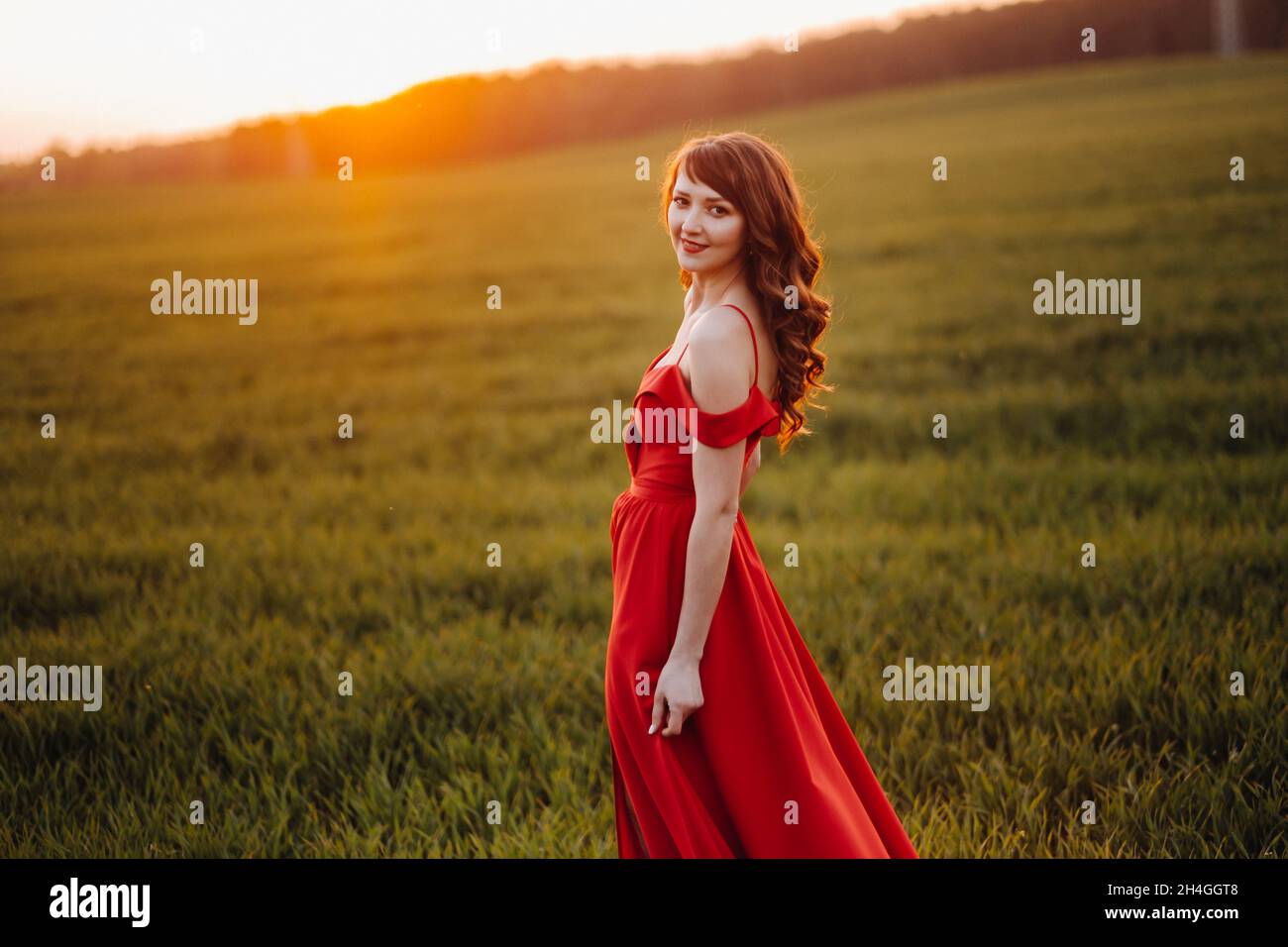 a beautiful girl in spring in a red dress is walking in a field at ...