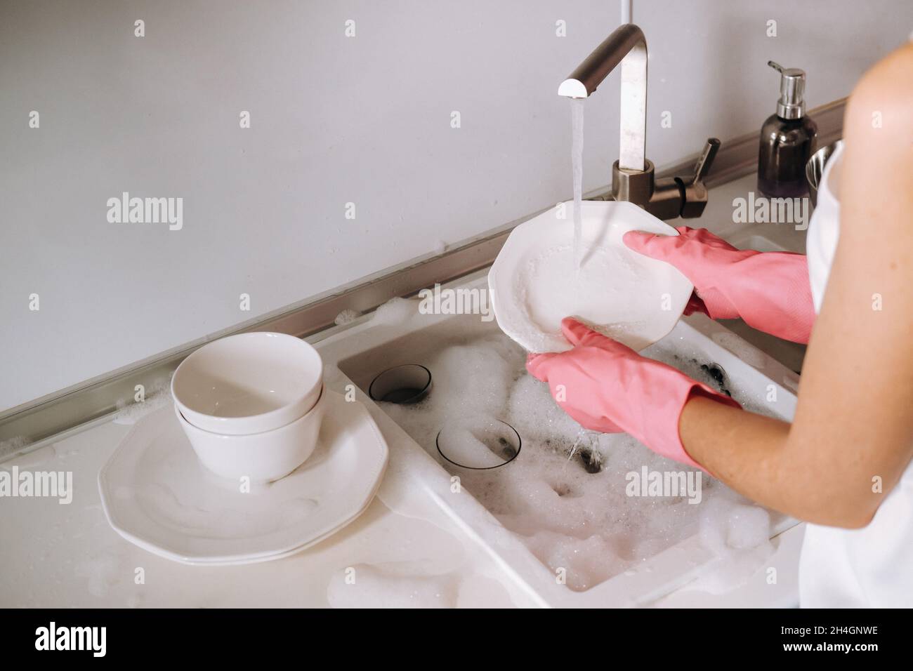 housewife girl in pink gloves washes dishes by hand in the sink with detergent. The girl cleans the house and washes dishes in gloves at home Stock Photo