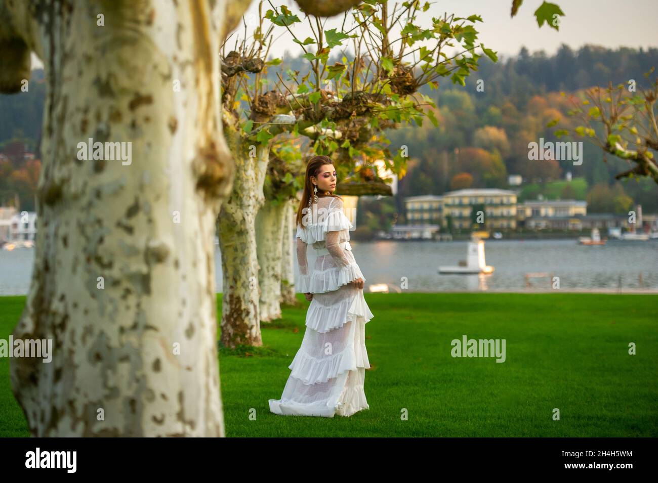 A bride in a white wedding dress in a park in an Austrian town with large trees at sunset. Stock Photo