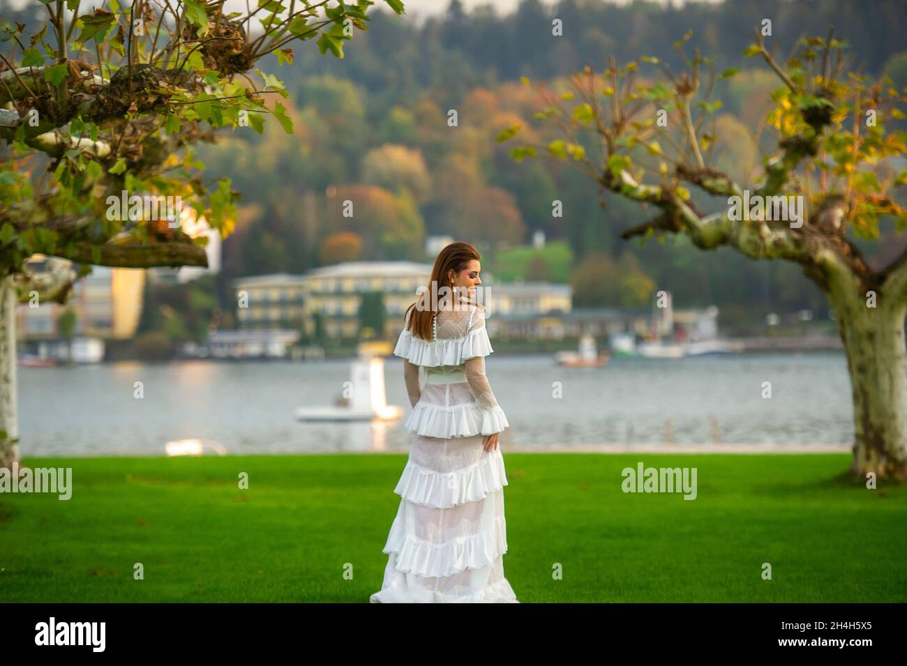 A bride in a white wedding dress in a park in an Austrian town with large trees at sunset. Stock Photo