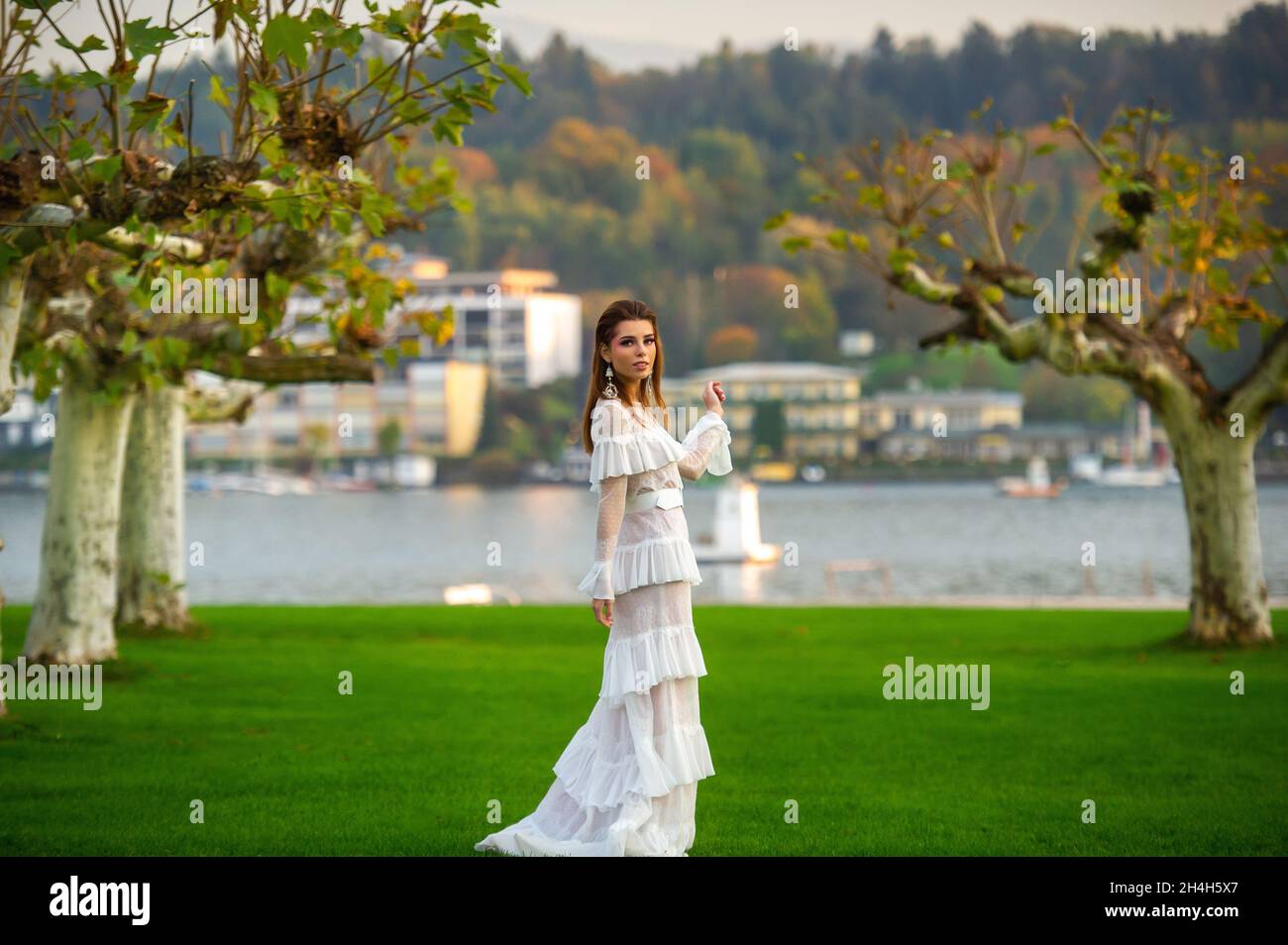 A bride in a white wedding dress in a park in an Austrian town with large trees at sunset. Stock Photo