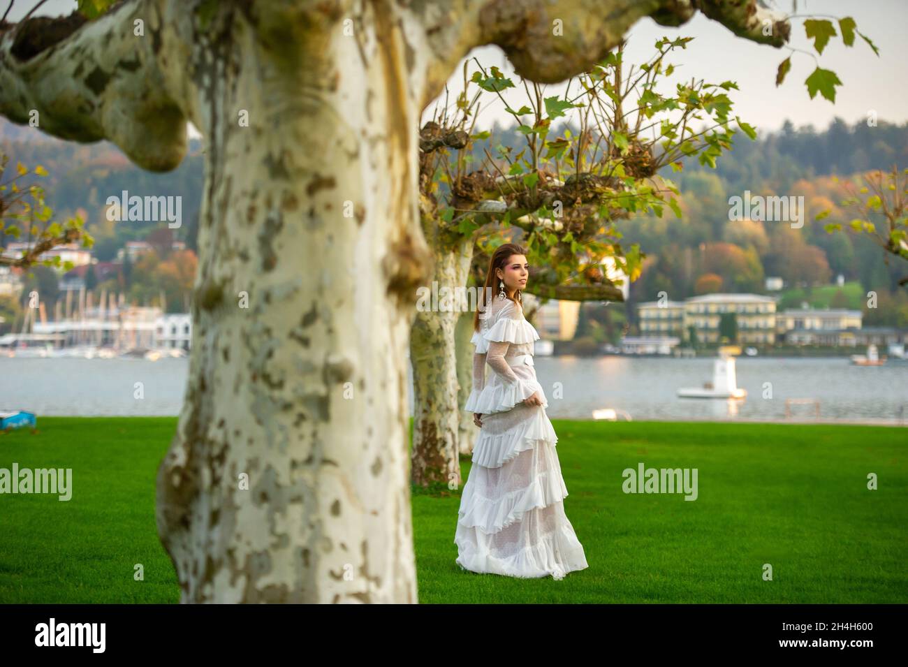 A bride in a white wedding dress in a park in an Austrian town with large trees at sunset. Stock Photo