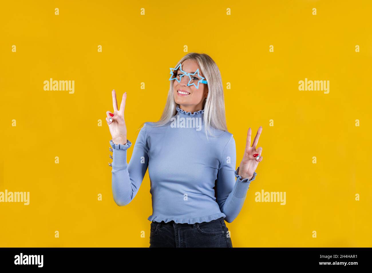 Portrait of an attractive trendy cheerful girl wearing star shape sunglasses and showing peace or victory sign. Close-up of beautiful woman Stock Photo
