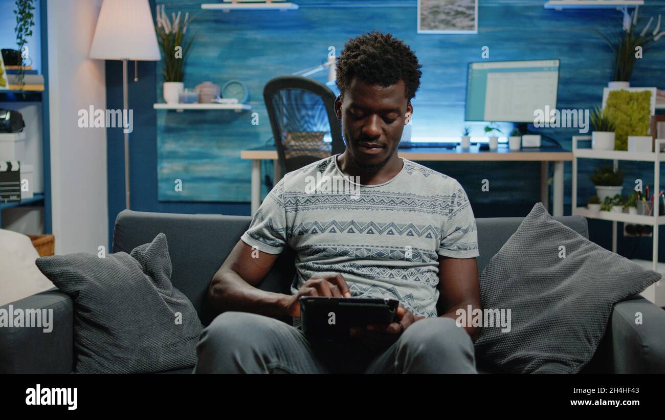 Young freelancer using digital tablet with touch screen for work online. Person with entrepreneur job holding gadget and working from home with modern technology. Man using internet Stock Photo