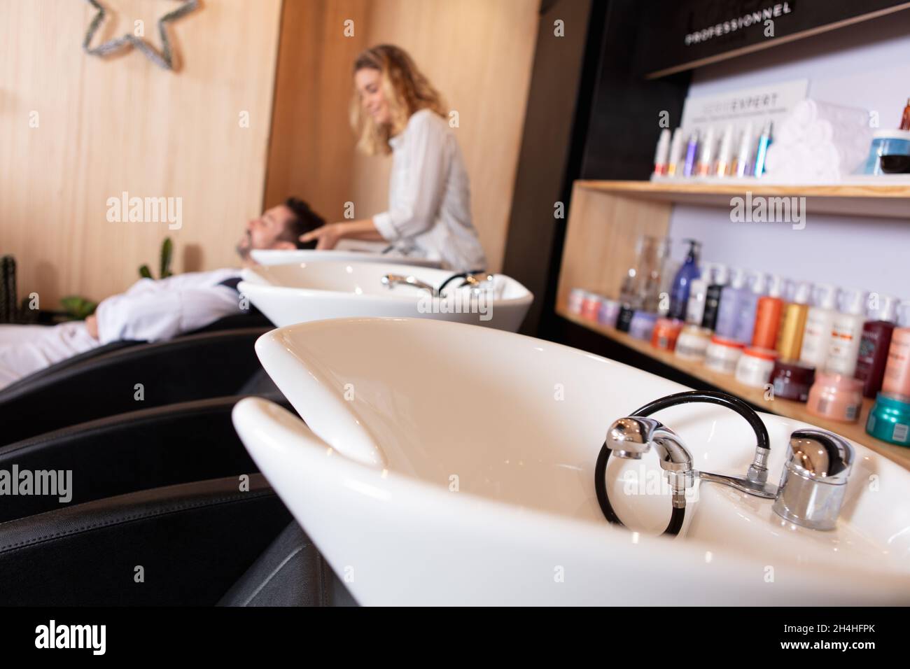 view of sinks and hairdresser washing clients hair in salon Stock Photo