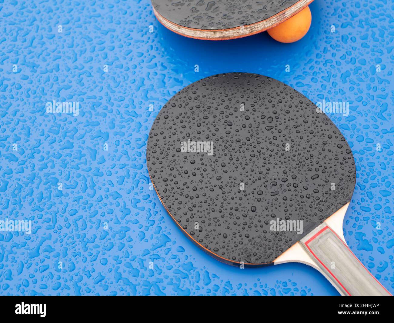 Ping-Pong paddles and ball, that were left during the rain. Table tennis. Sports equipment on the ping pong table Stock Photo