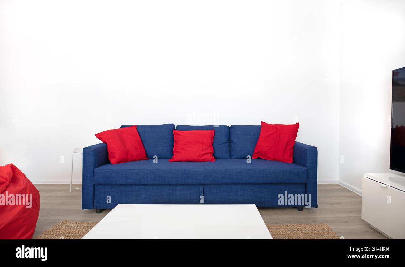 Blue sofa with red cushions in front of white wall Stock Photo