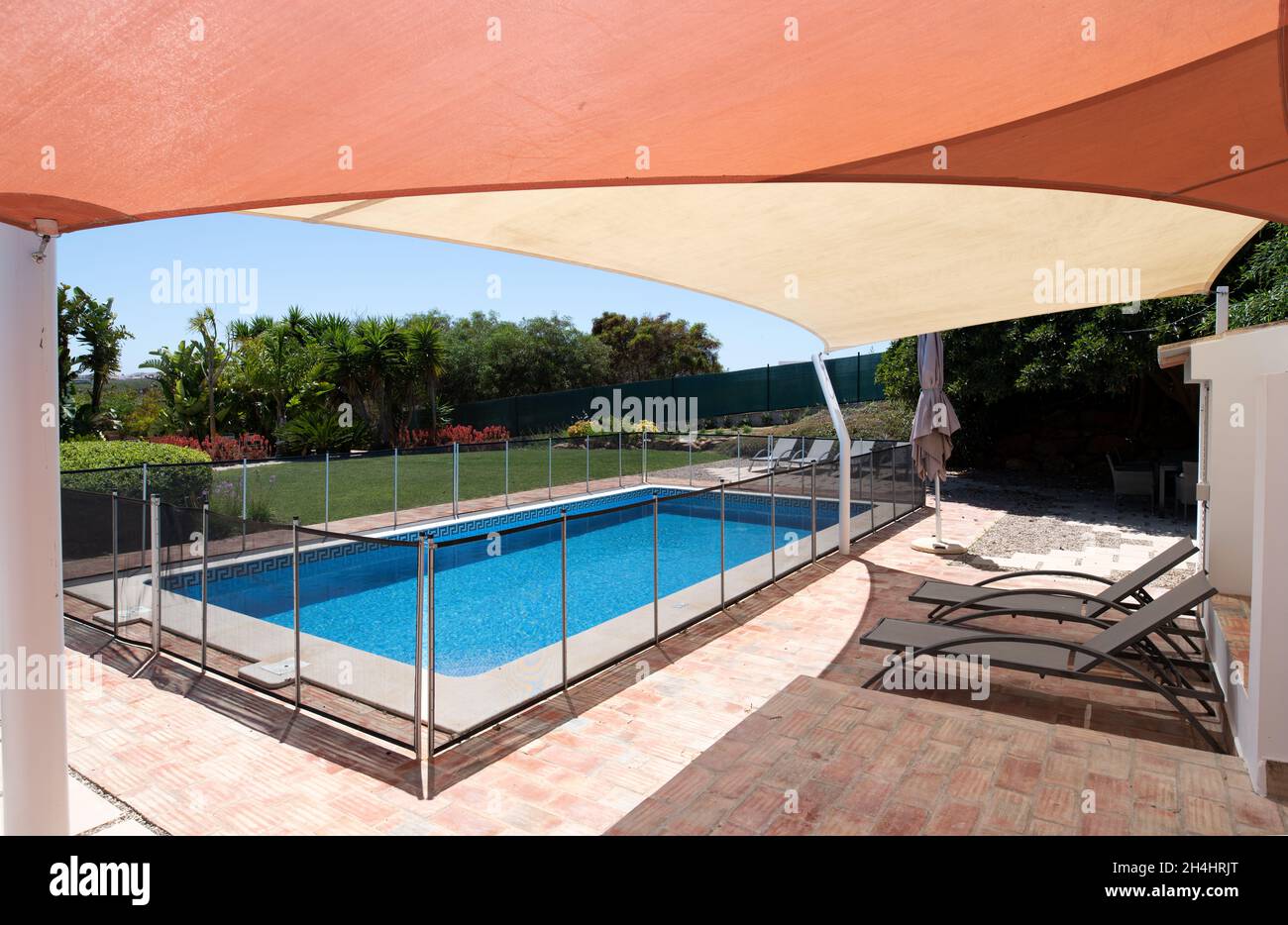 Fenced swimming pool in garden with sunbeds under a shade sail Stock Photo