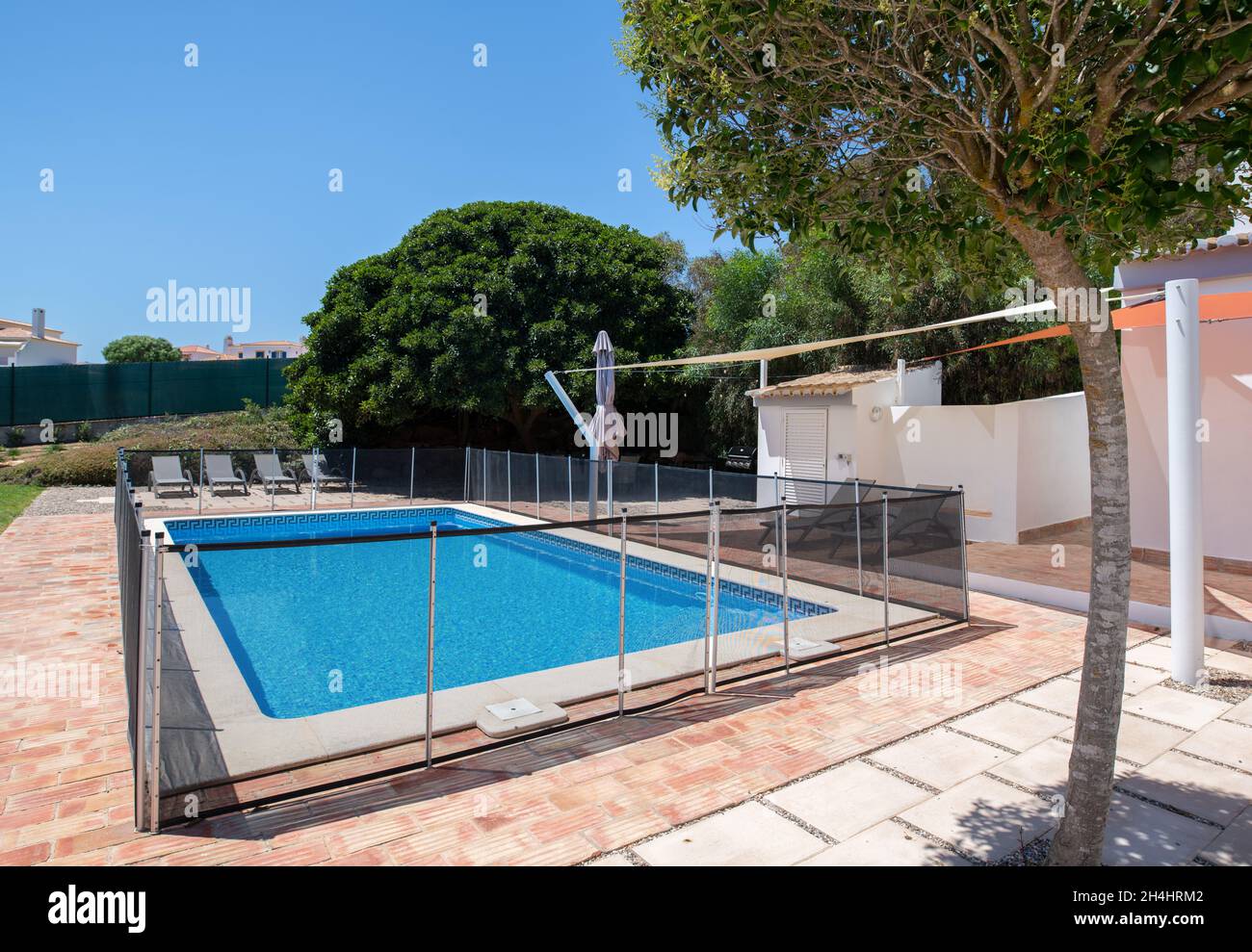 Fenced swimming pool with brick tiled surround in the garden of a white villa Stock Photo