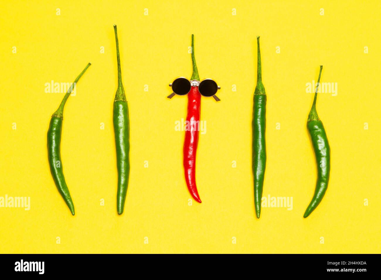 Red chili pepper in sunglasses surrounded by green peppers. The coolest guy, party goer bright funny concept Stock Photo
