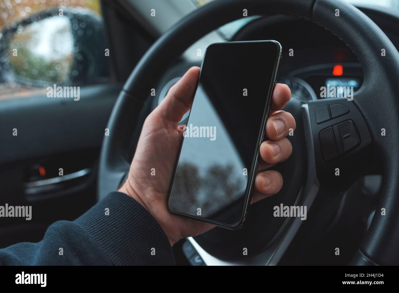 Car driver holding mobile smart phone over steering wheel, blank black screen as copy space, selective focus Stock Photo