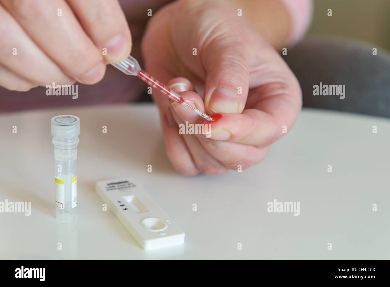 The woman takes a blood sample with a pipette from his finger to perform a COVID19 test Stock Photo
