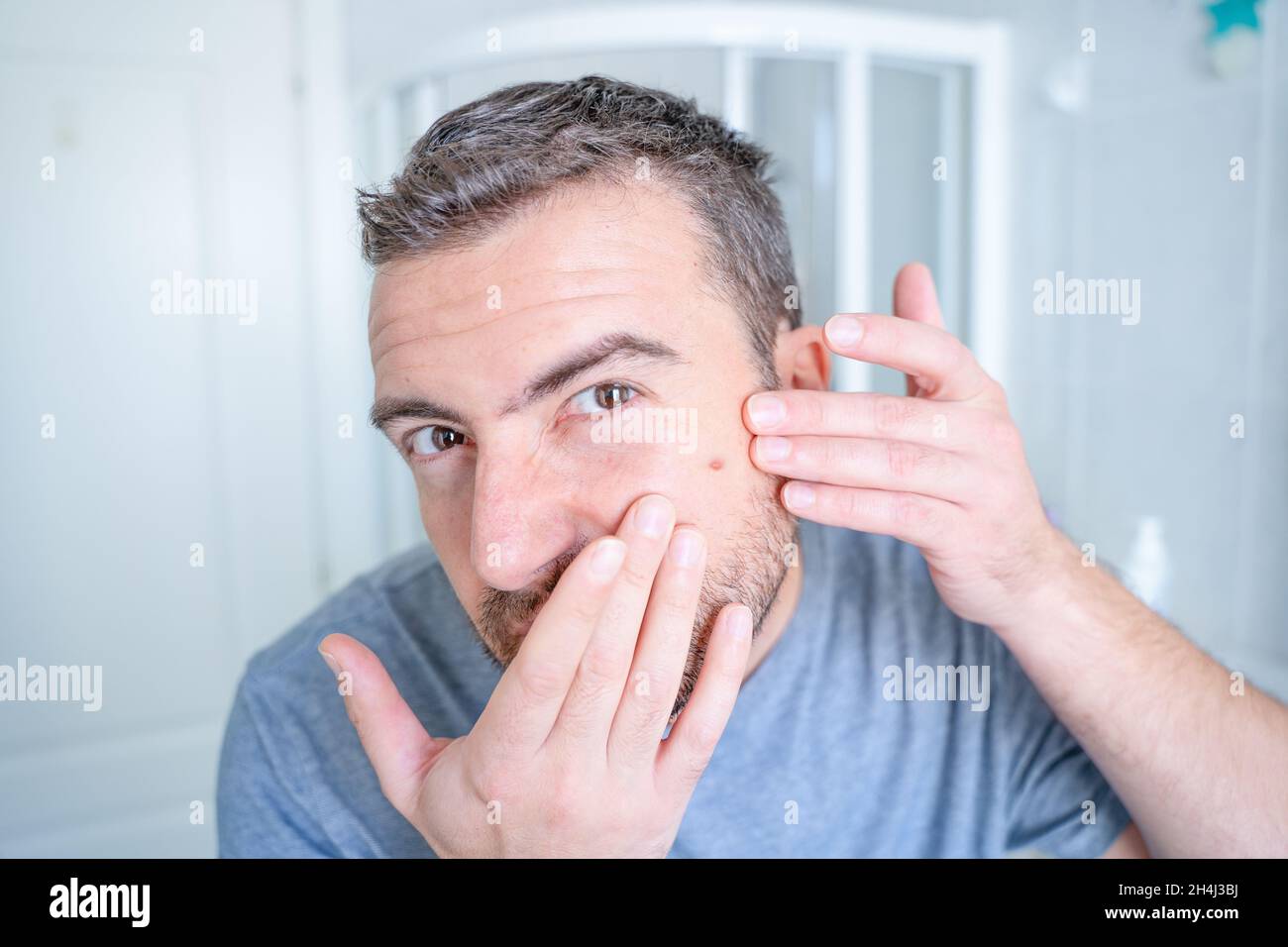 Man popping a pimple looking in the mirror Stock Photo