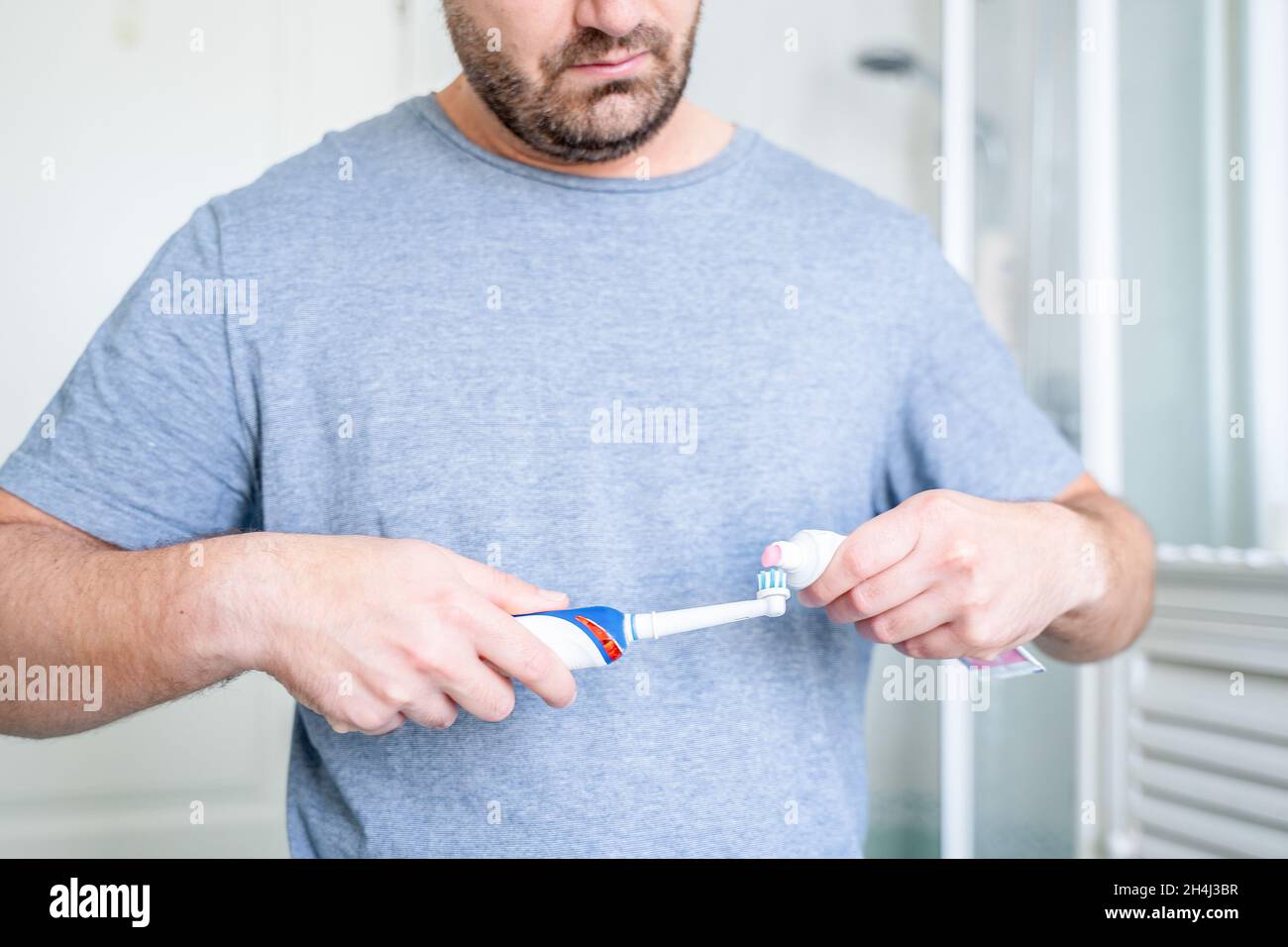 Man putting toothpaste on electric toothbrush in bathroom Stock Photo