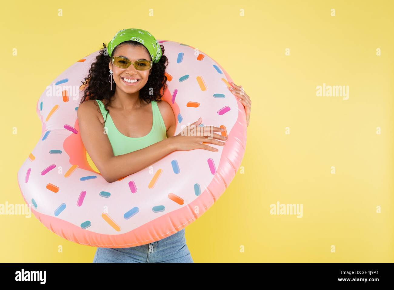 positive african american young woman standing with inflatable ring isolated on yellow Stock Photo