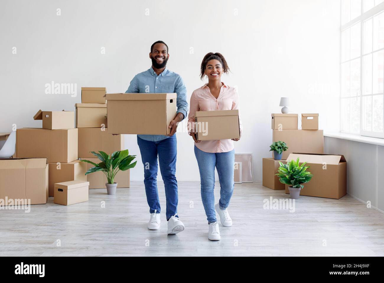 Smiling millennial african american husband and wife carry boxes of ...