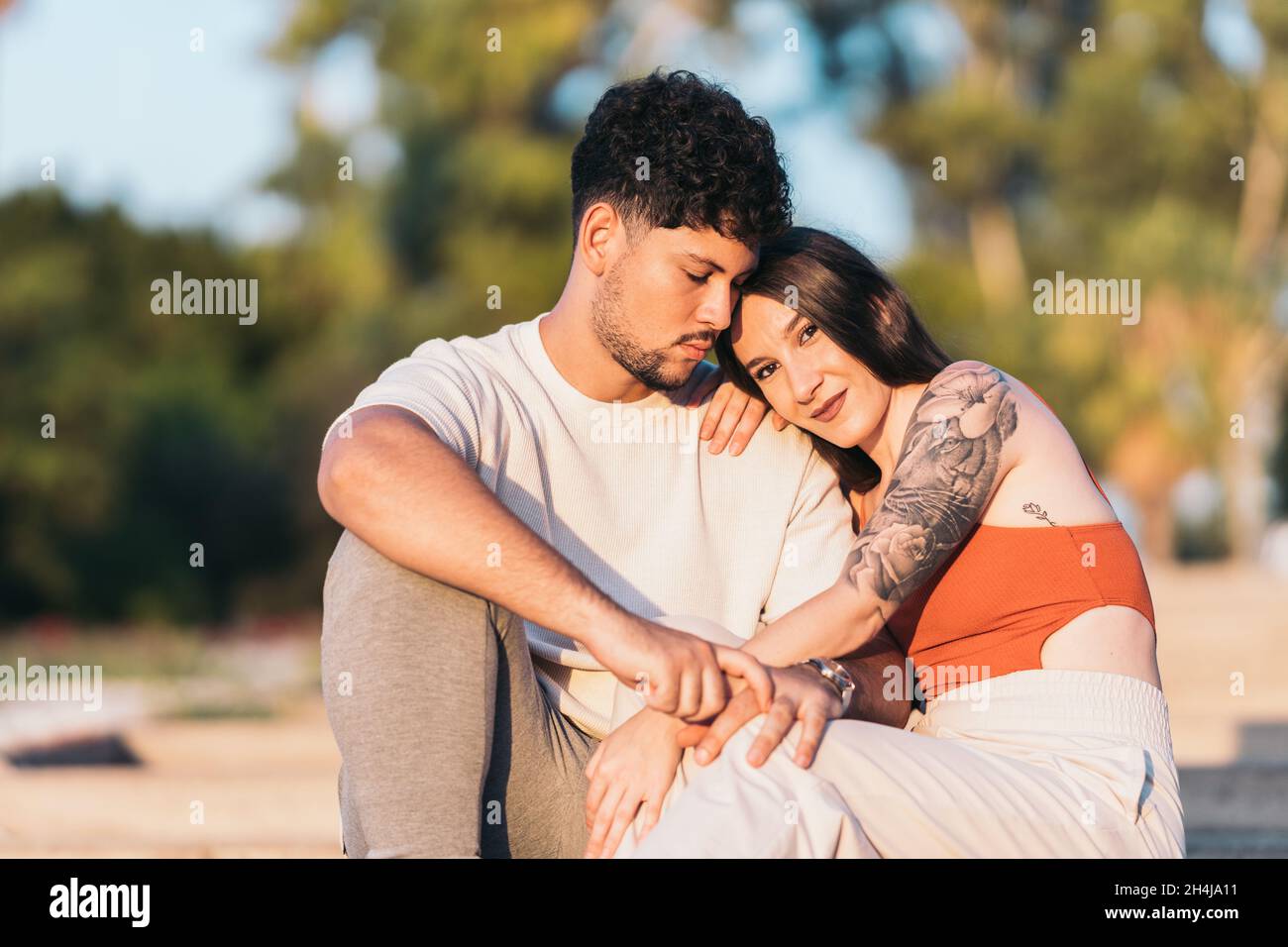 Couple embraced while sitting on a park during sunset Stock Photo