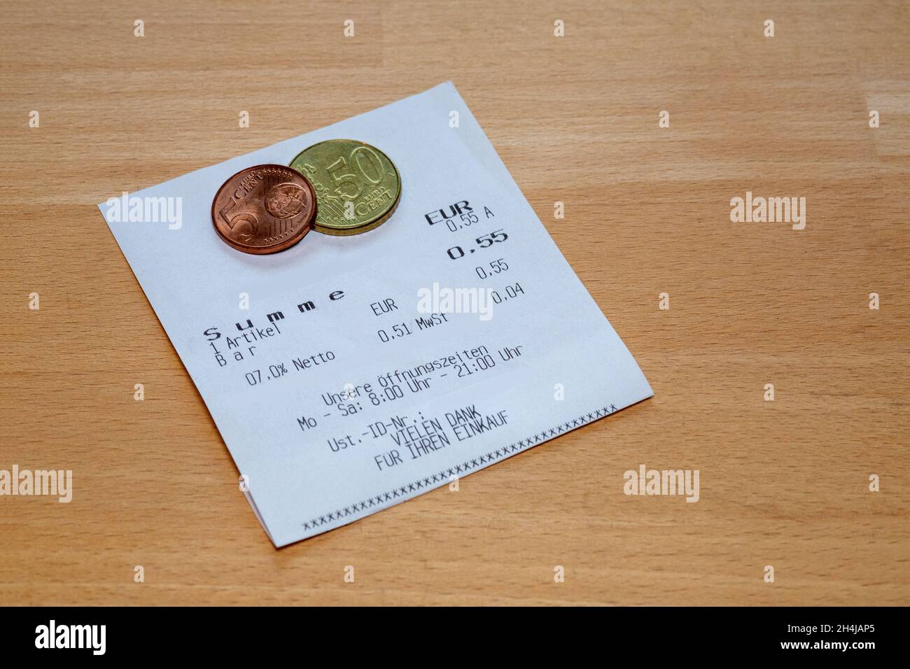 Printout of a receipt on wooden table with small euro coins The receipt contains the German words for: Sum, items, cash, net, VAT, VAT ID no., our ope Stock Photo