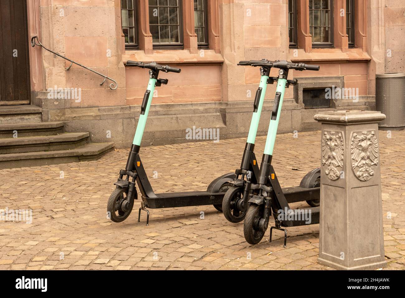 After use, three e-scooters are parked in front of a historic building in the middle of the city Stock Photo