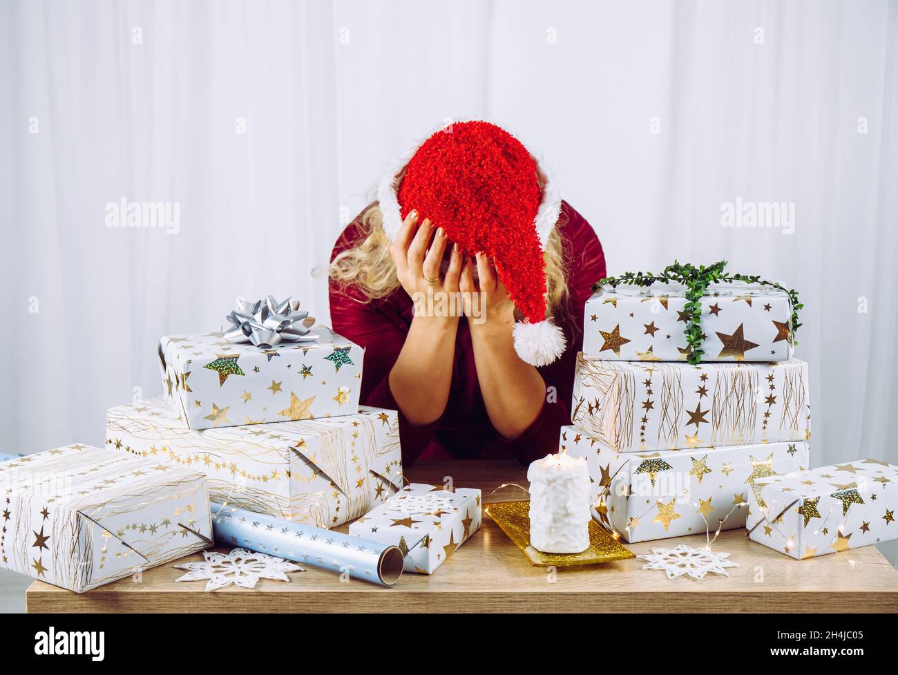 Unrecognizable woman housewife tired of wrapping Christmas presents in home. Stacks of gifts. Seasonal holidays depression concept. Stock Photo