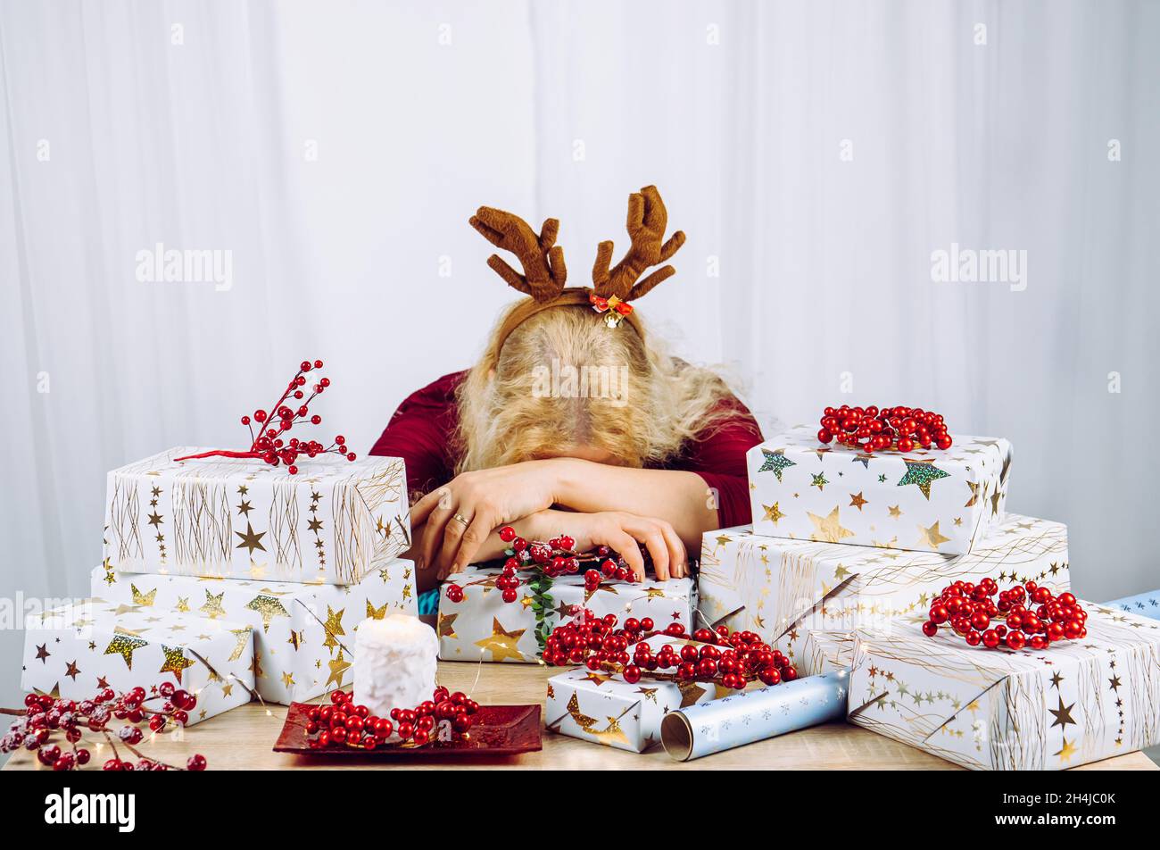 Unrecognizable woman housewife tired of wrapping Christmas presents in home. Stacks of gifts. Seasonal holidays depression concept. Stock Photo