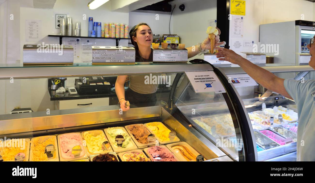Young woman at historic ice cream counter in Henley-in-Arden high street serving customer double cone of ice-cream, UK Stock Photo