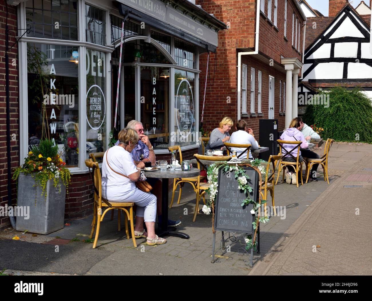 Eating food at tables on pavement outside deli, takeaway, cafe, bakery shop in Henley-in-Arden, Warwickshire, UK Stock Photo