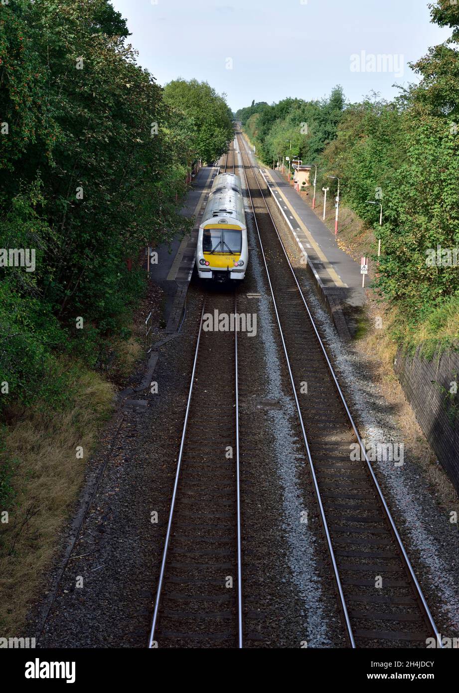 Short, two carriage, commuter train passing deserted platform in straight section of double rails, UK Stock Photo