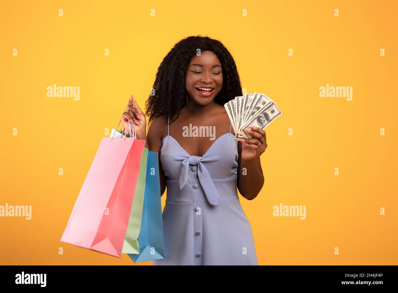 Shopping budget. Portrait of young black woman holding fan of money and colorful shopper bags over orange background Stock Photo