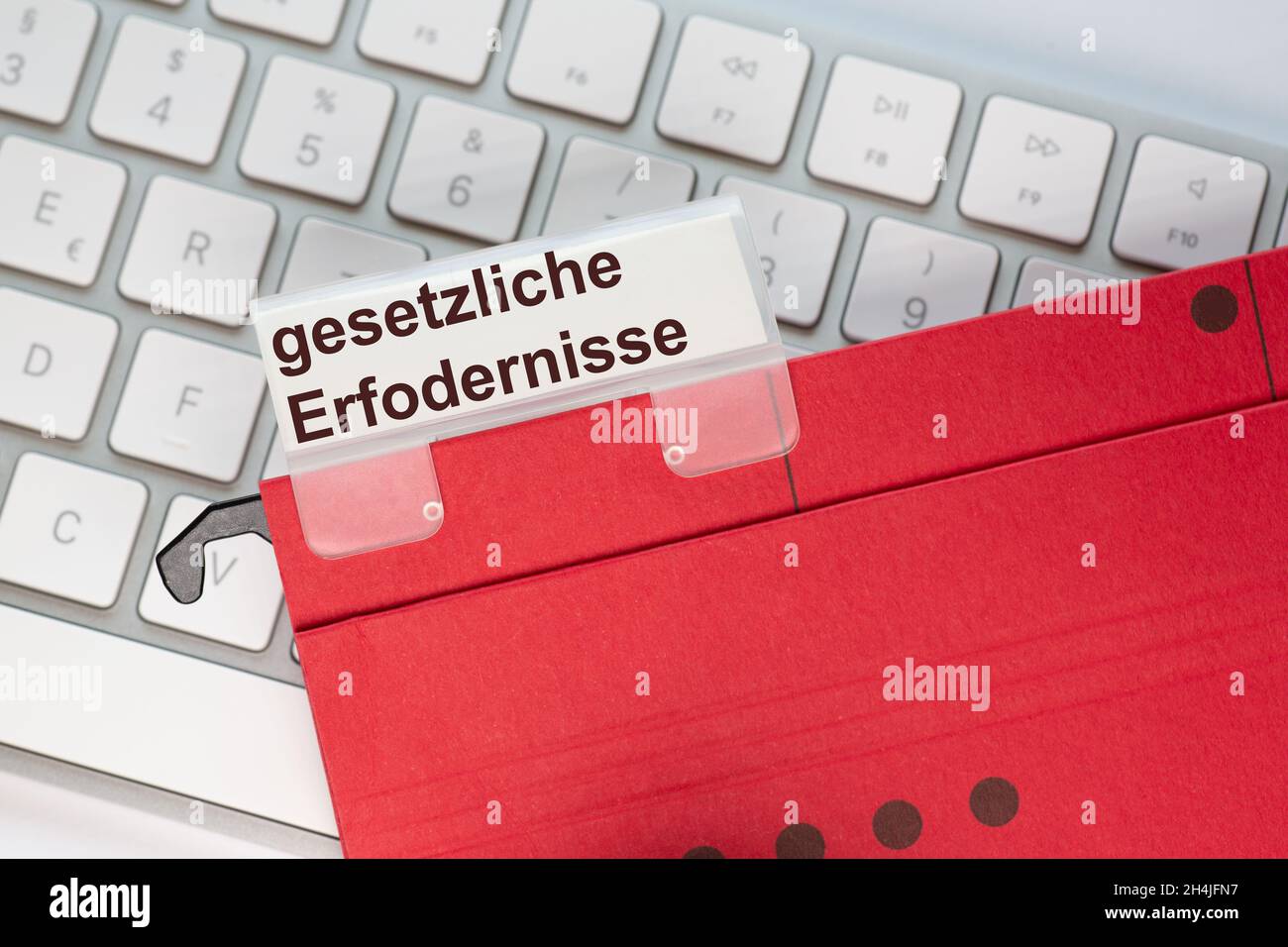 The German words for legal requirements can be seen on the label of a red hanging folder. The hanging folder is on a computer keyboard. Stock Photo