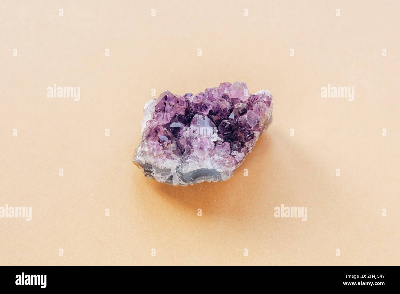 Purple amethyst crystal on a light beige background, close up. Top view. Stock Photo