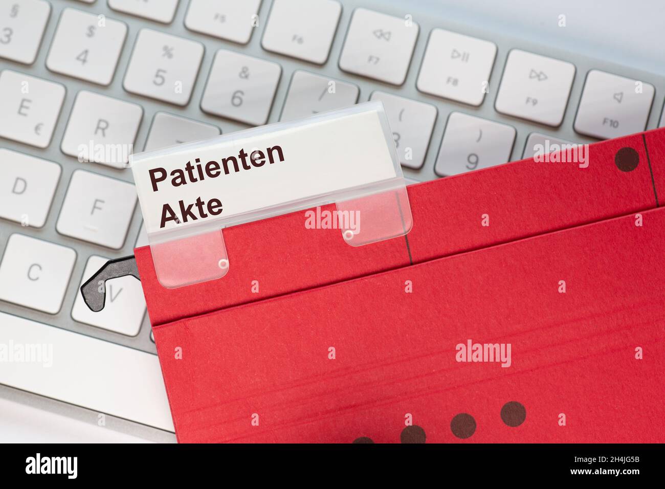 The German word for Patient file can be seen on the label of a red hanging folder. The hanging folder is on a computer keyboard. Stock Photo