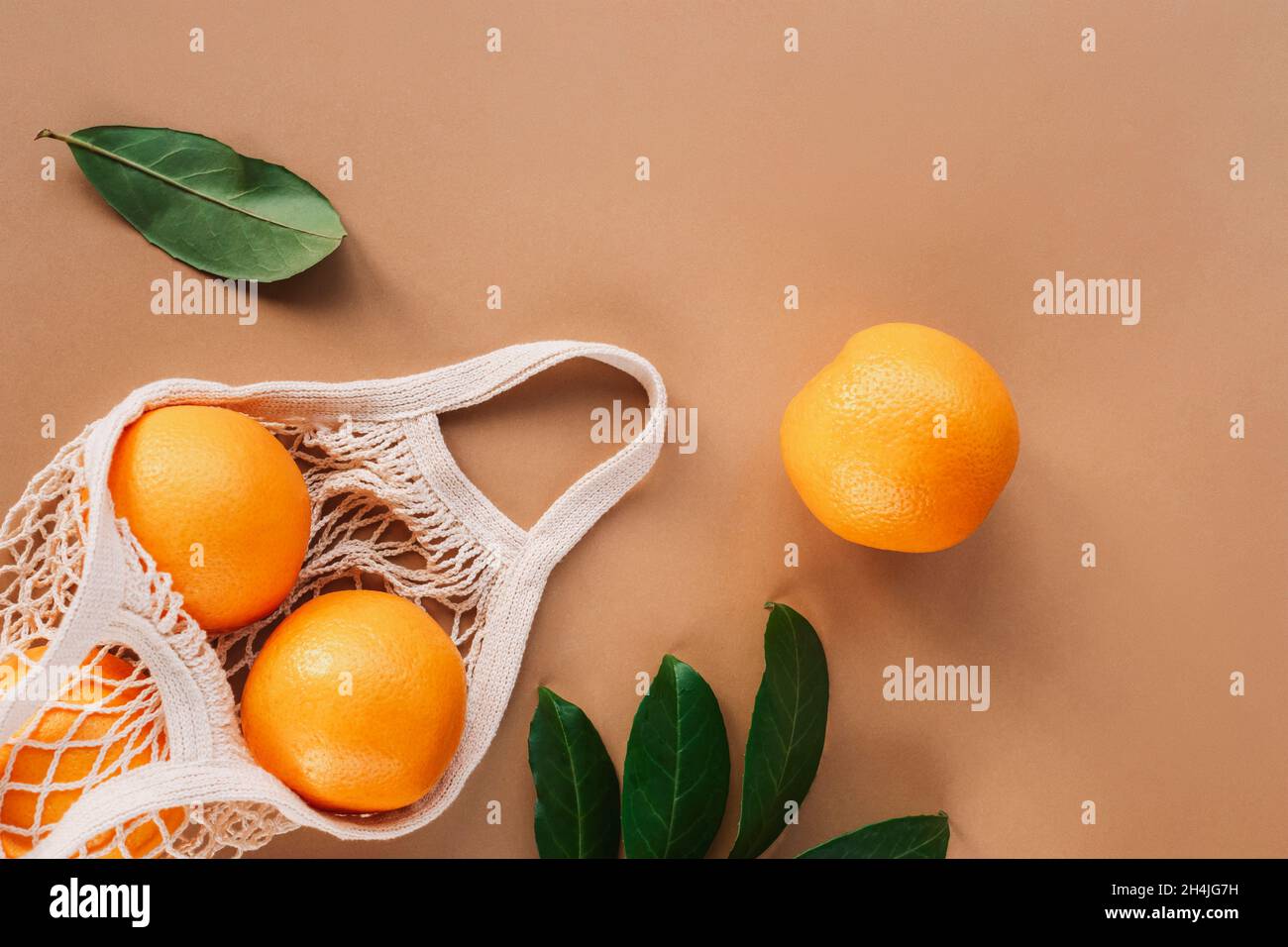 https://c8.alamy.com/comp/2H4JG7H/oranges-in-a-string-bag-with-green-leaves-on-tan-beige-background-top-view-flat-lay-2H4JG7H.jpg