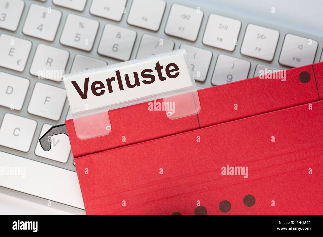 The German word for losses can be seen on the label of a red hanging folder. The hanging folder is on a computer keyboard. Stock Photo