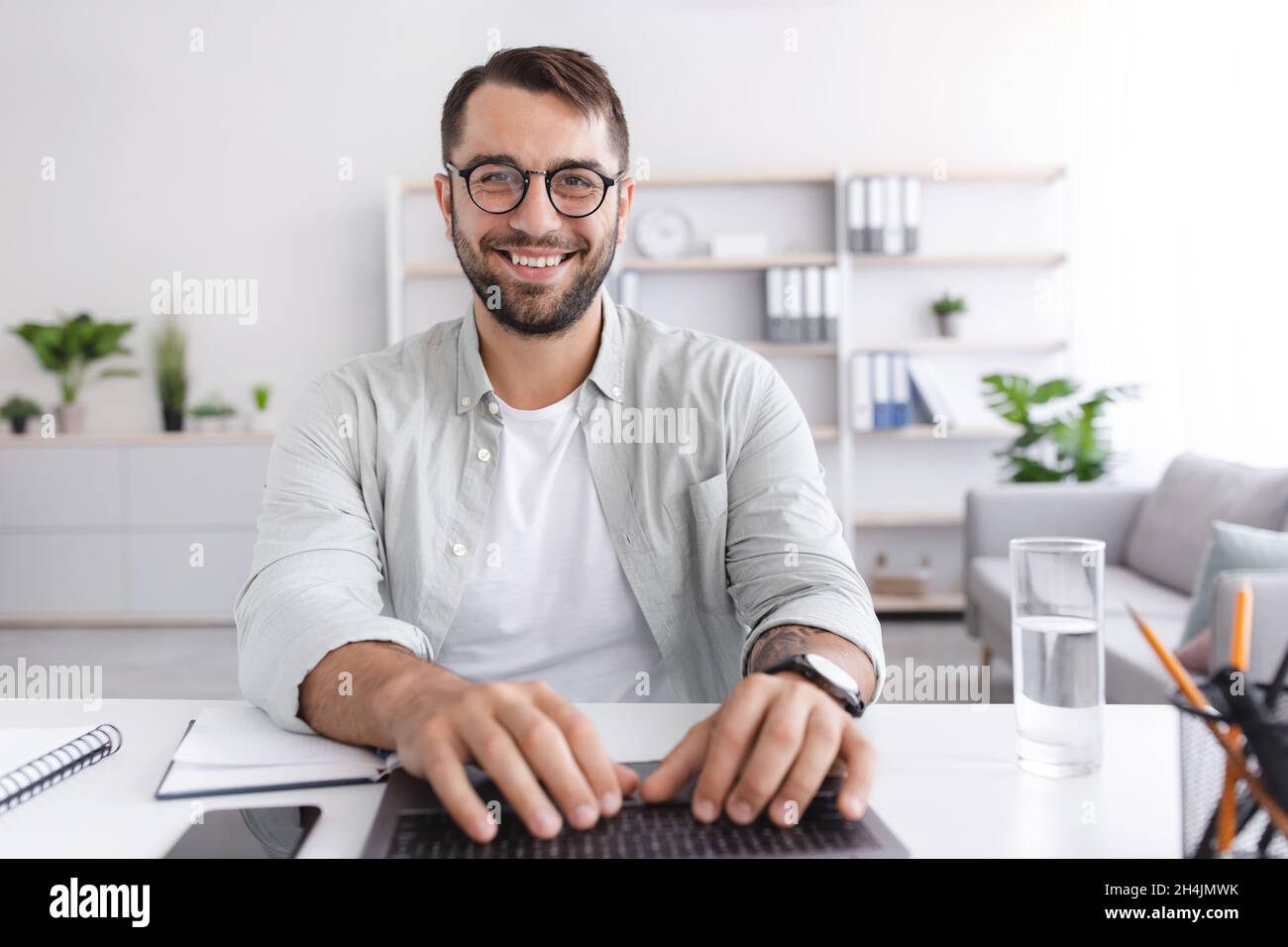 Cheerful mature caucasian guy in glasses working on laptop or have online meeting on living room interior. Communication remotely, video call, meeting Stock Photo