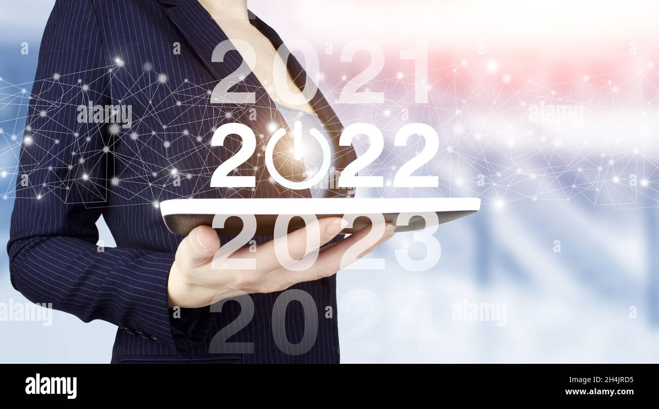 Concept Start New Year 2022. Hand hold white tablet with digital hologram 2022 sign on light blurred background. Happy New Year 2022 - New year 2022, Stock Photo