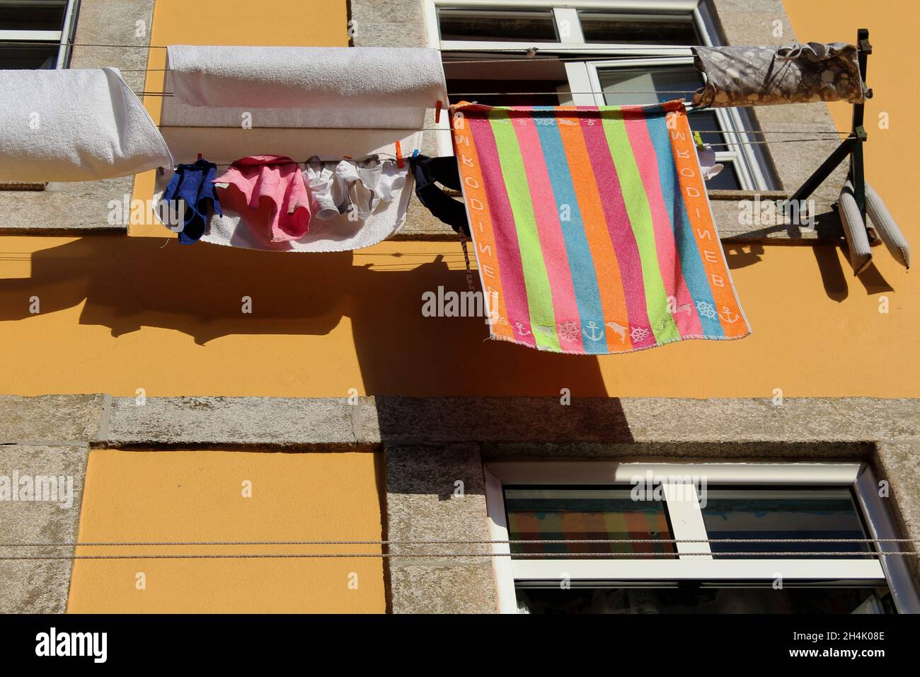 Bunte Wäsche trocknet in der Sonne an einer Wäscheleine, die an einer gelben Hauswand angebracht ist in Porto, Portugal. Stock Photo