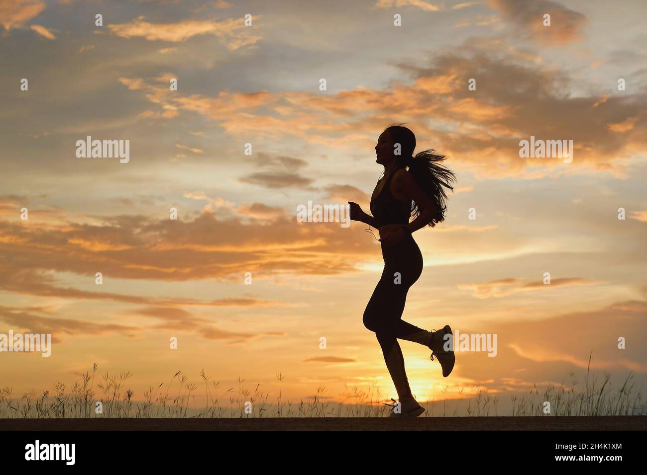 Silhouette of a woman jogging at sunset, Thailand Stock Photo