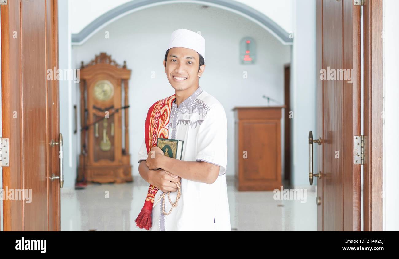 Portrait of a smiling man standing in a mosque holding prayer beads and the quran after prayers Stock Photo