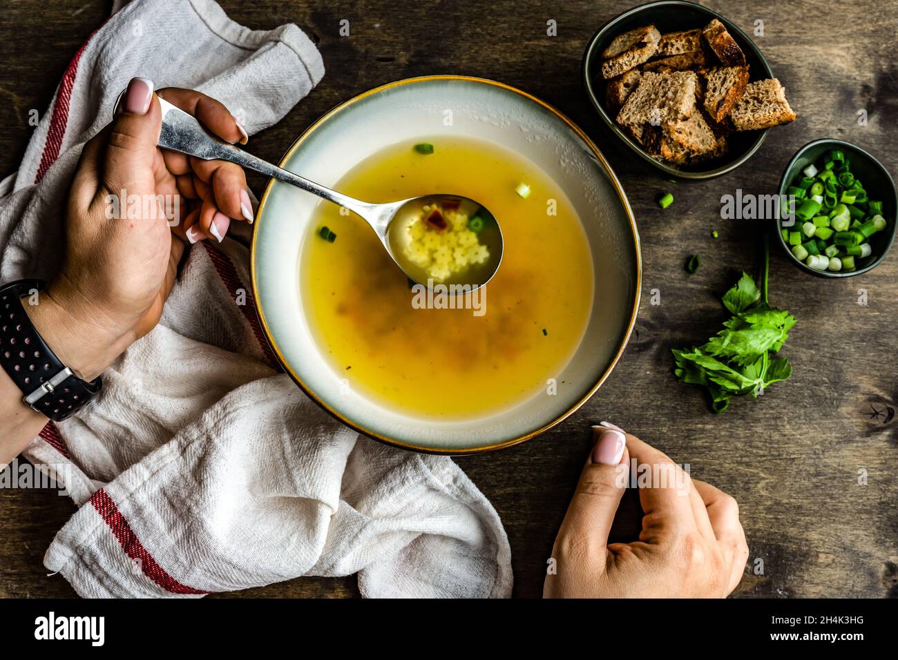 Woman eating a bowl of healthy chicken broth with pasta, croutons, parsley and spring onions Stock Photo