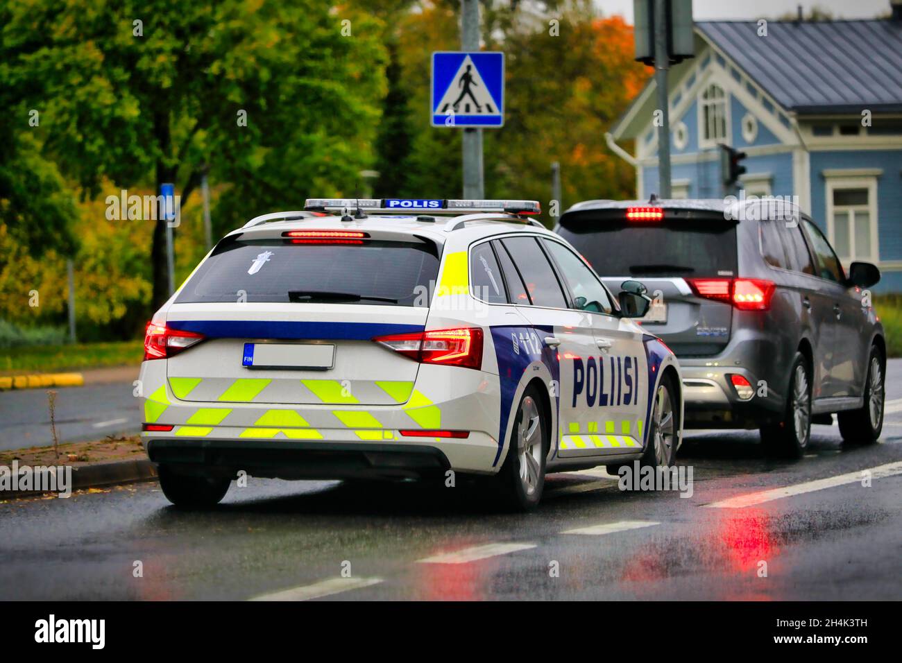 Police vehicle travelling behind car on city street, lined up to take left turn on a rainy day of autumn. Salo, Finland. October 24, 2021 Stock Photo