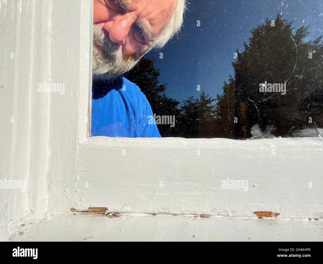 Outdoor view of a Senior man standing indoors peering out of a window Stock Photo