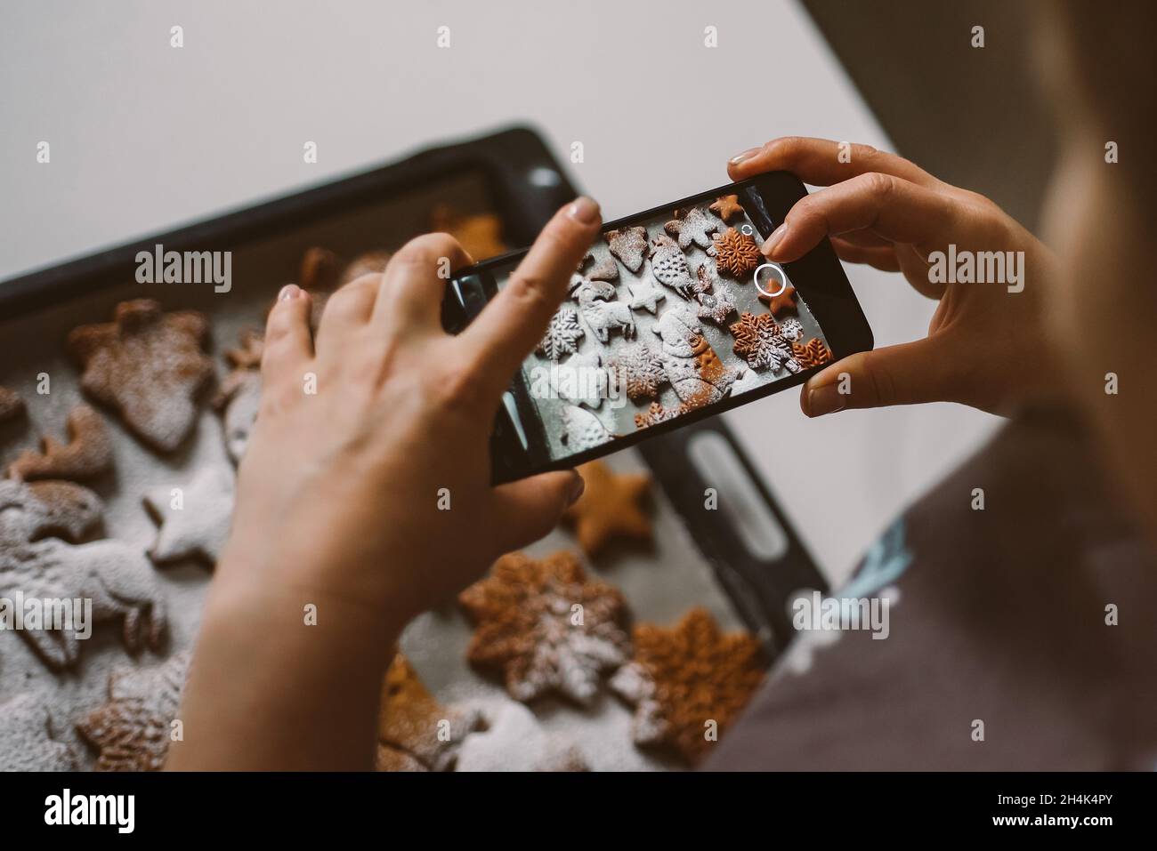 Woman takes photo on smartphone Christmas gingerbread sprinkled with powdered sugar. Stock Photo