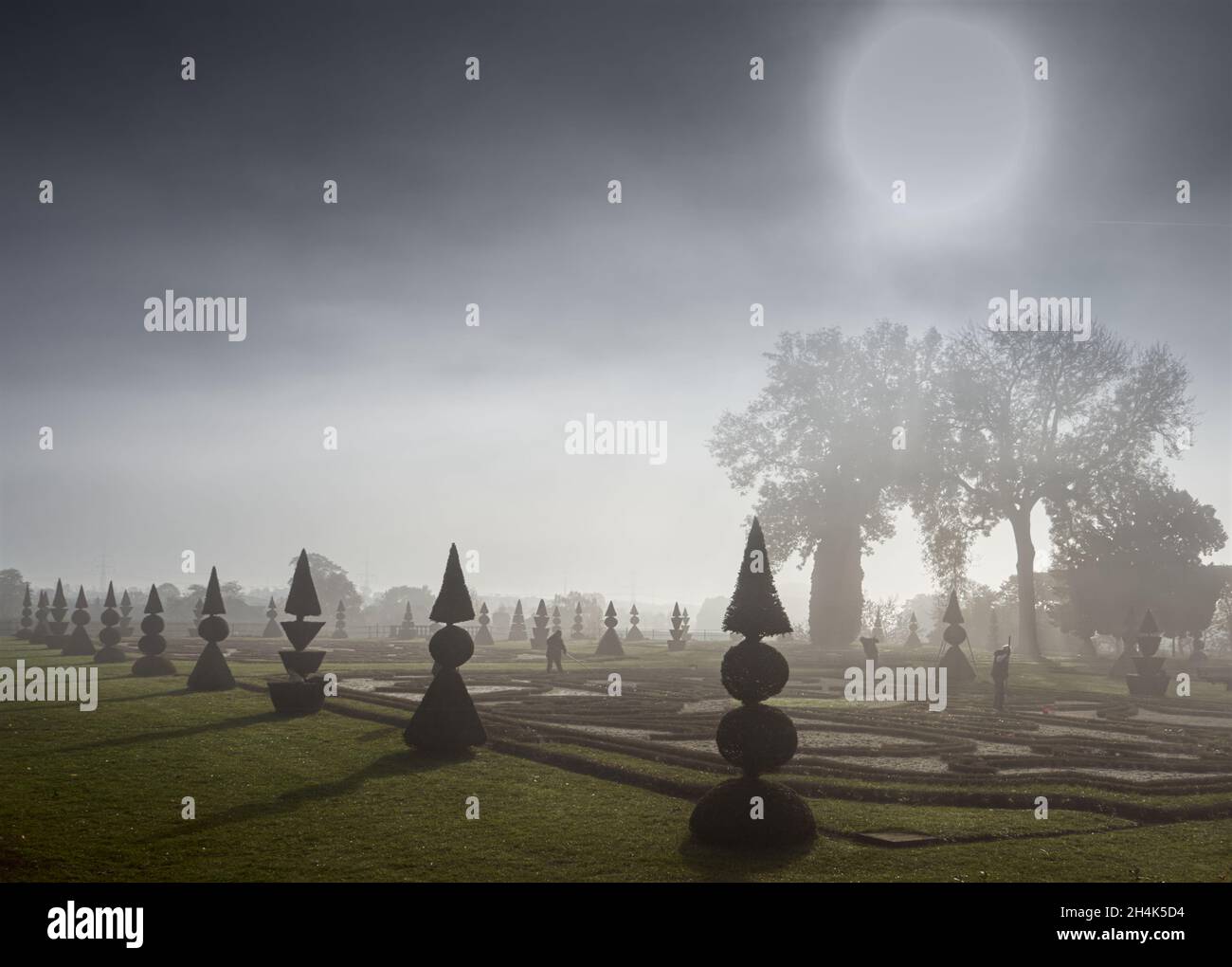 Sun disk above fog over baroque garden with gardeners not recognizable Stock Photo
