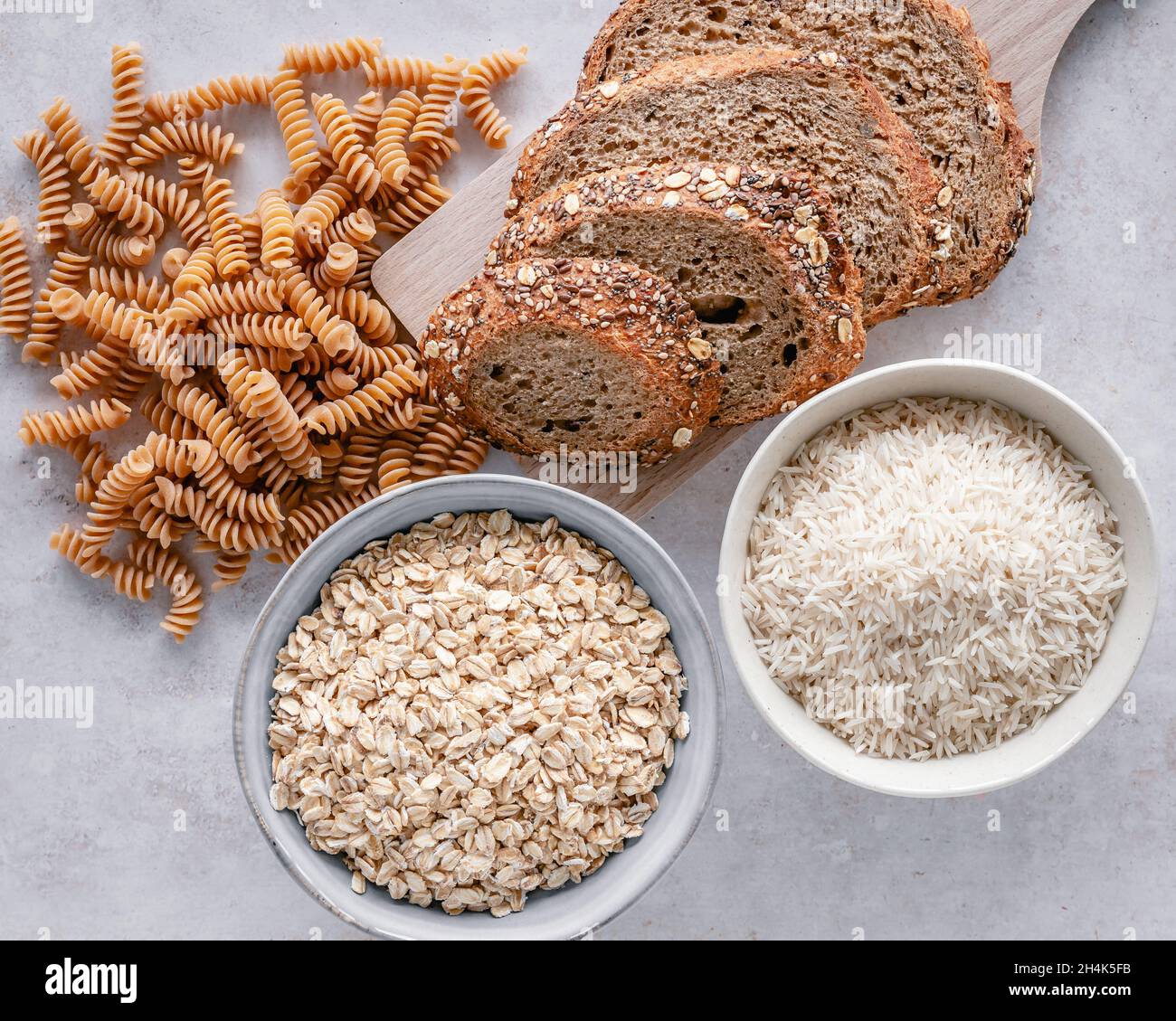 Overhead view of wholegrain pasta, wholegrain sourdough, rolled oats and long grain rice on a table Stock Photo