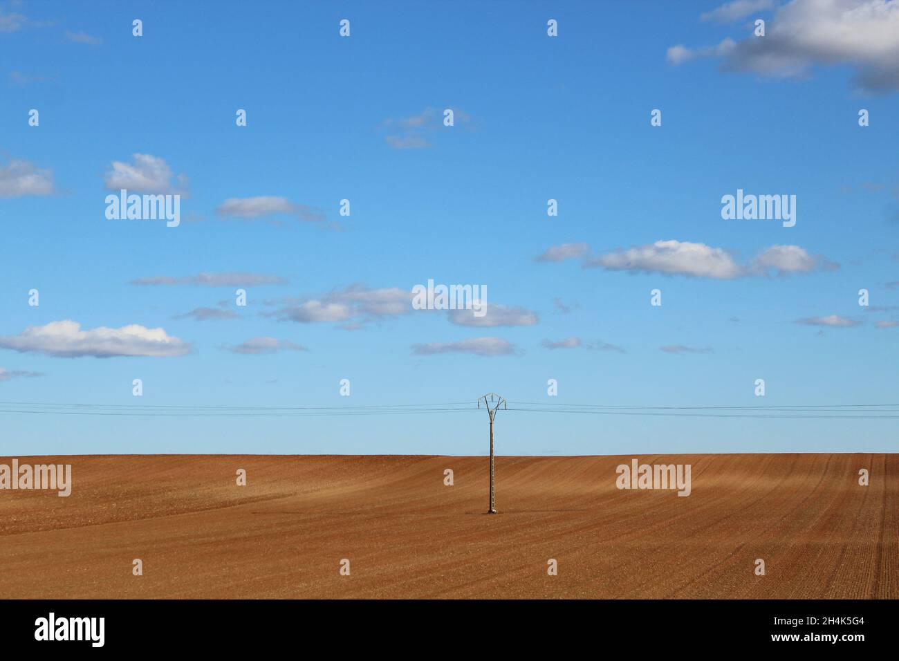 Landschaftsbild: ein braunes, abgemähtes Feld mit einem Strommast, blauer Himmel und Wolken in Spanien - kurz vor der Grenze zu Frankreich. Stock Photo